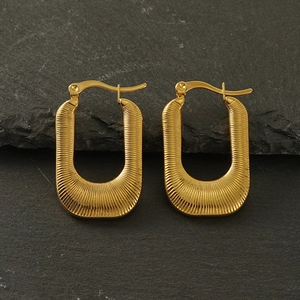 Macro detail of gold U-shaped earrings with ribbed texture on a grey slate background