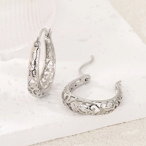 Detail view of silver hoop earrings featuring hollow heart patterns on a marble surface