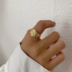 Detail of a textured gold signet ring featuring a unique irregular molten lava surface