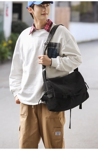 Close-up of black canvas messenger bag showing adjustable strap and plastic buckle detail