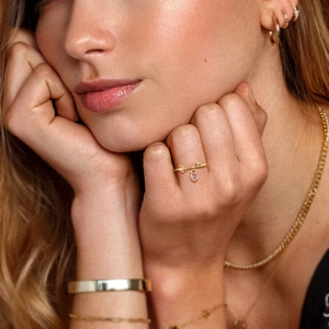 Detail of a gold ring featuring a pink heart pendant and clear gemstone charms on a finger