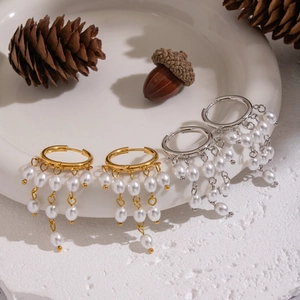 Elegant gold and silver hoop earrings with pearl tassels on a white ceramic display plate