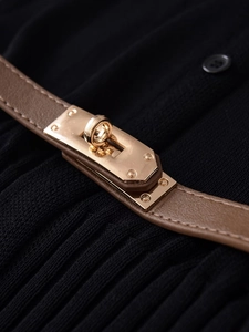 Macro view of gold metal turn-lock closure on brown leather belt with black knit fabric