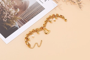 Détail d'un bracelet double épaisseur doré orné de pendentifs cœur et de perles blanches