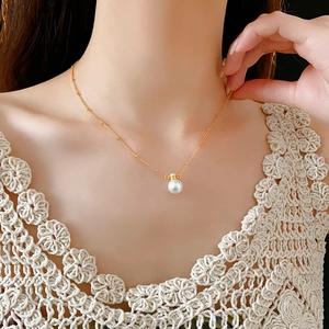 Close-up of golden necklace with a white pearl pendant on a woman's neck and collarbone