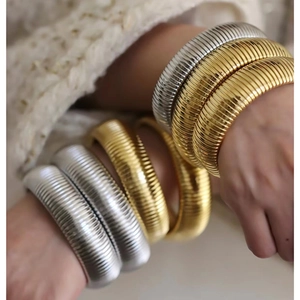 Dettaglio di bracciali Tubogas larghi oro e argento indossati sopra un maglione beige