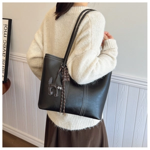 Back view of model wearing a large black leather tote bag with a cat charm and rope detail