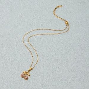 Detailed macro view of gold cherry pendant featuring pink gemstones and textured leaves