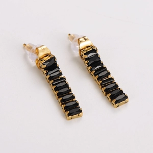 Detail of gold rectangular bar earrings with black square zircons on white background
