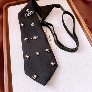 Close-up of black necktie with metal Saturn orb and cross charms on wood tray