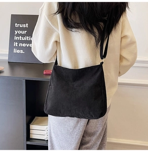 Detail view of black corduroy crossbody bag worn by a model showing texture and fit