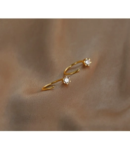 Detail view of gold hoop earrings with six-prong set clear zircon on warm silk fabric