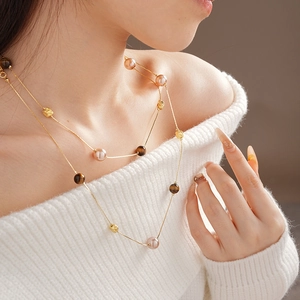 Detail of layered gold necklace with pink pearls and brown tiger eye beads on a model