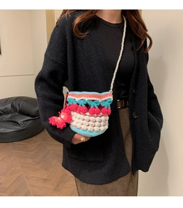 Detail of handmade knit bucket bag featuring a pearl strap and red butterfly charm