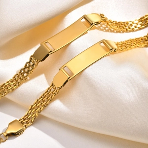 Macro shot of gold mesh ID bracelets on white silk focusing on the engravable bar