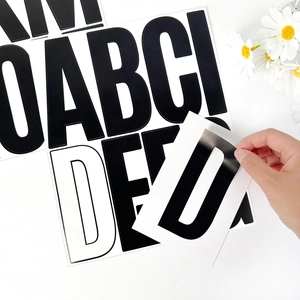 Hand peeling black 5-inch alphabet wall sticker from white backing on wood background