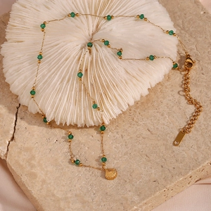 Detail of gold chain necklace with green faceted beads and shell pendant on stone