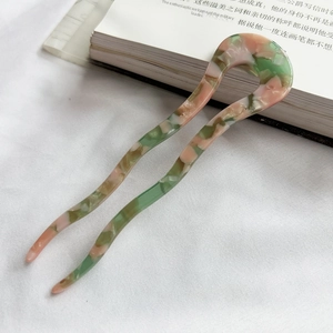 Detail of pink and green marbled acetate U-shaped hair pin on white fabric