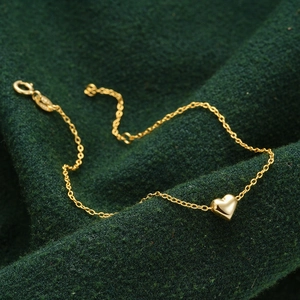 Detailed macro view of a 3D gold heart pendant on a delicate chain over green fabric