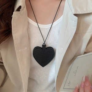 Close-up of black leather heart pendant with pebble texture on a minimalist cord necklace