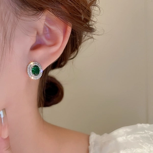 Close-up of a vintage oval green gemstone earring with sparkling diamond halo on model