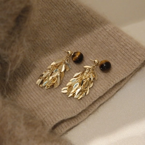 Detailed shot of golden leaf tassel earrings with tiger eye beads on knit fabric