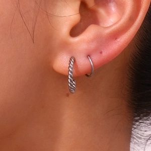Detail of twisted spiral and smooth silver steel hoop earrings on model ear lobe