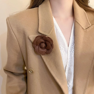 Detail of dark brown leather flocking flower brooch on a camel wool coat lapel