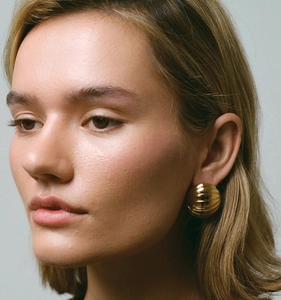 Close-up of golden ribbed oval earrings on model showing shell texture and metallic luster
