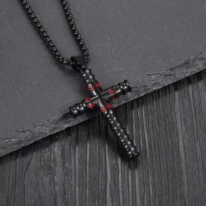 Collier avec pendentif croix cylindrique en métal noir et détails rouges sur fond sombre