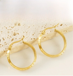 Macro view of gold hoop earrings with Greek key pattern on textured stone