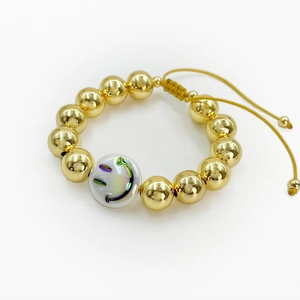 Detail of adjustable gold beaded bracelet with a white iridescent smiley face bead