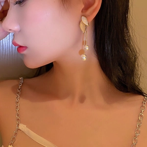 Close-up of elegant gold leaf and pearl tassel earrings worn by a model