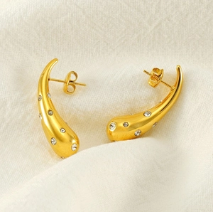 Detail of gold teardrop earrings with inlaid white zircons on white textured fabric