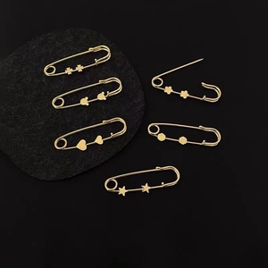 Golden metal safety pins with heart and star patterns on black background for waist adjustment