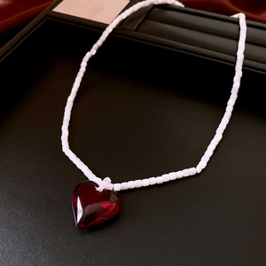 Close-up of a red heart pendant on a white square beaded necklace over black leather
