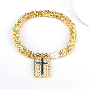 Detail of gold beaded bracelet with a pavé rectangle cross charm and an irregular white pearl