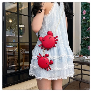 Model wearing a red crab-shaped mini crossbody bag set with gold chain on white dress