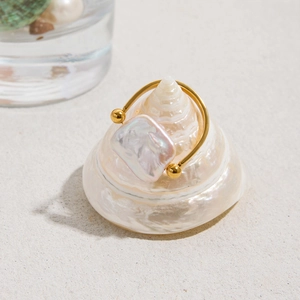 Macro view of a square freshwater pearl on a golden stainless steel ring on a seashell