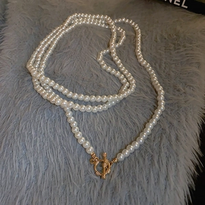 Detail of multi-layer pearl necklace with textured golden OT clasp on soft gray background