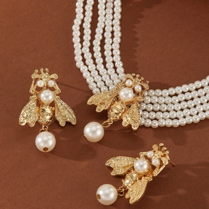 Golden bee necklace and earrings set with layered pearls on warm brown background