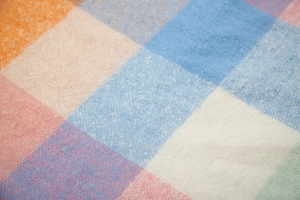 Macro view of checkered knit scarf featuring vibrant orange, blue, and white weave texture