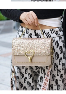 Detail of beige shoulder bag with gold sequins, heart clasp and dual woven strap