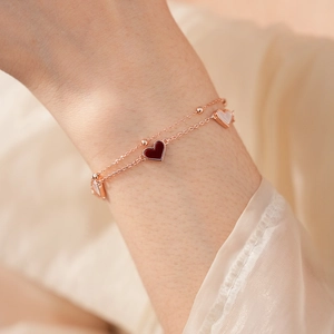Bracelet double couche en or rose avec pendentifs cœurs porté au poignet d'une femme