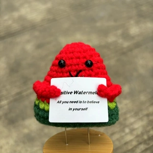 Macro shot of a handmade crochet watermelon doll holding an encouraging white card
