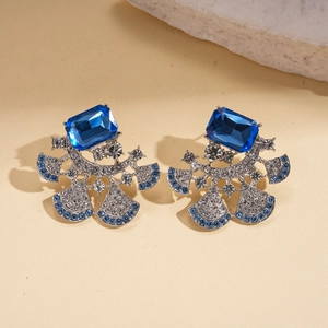 Macro shot of silver needle earrings featuring blue square gems and fan-shaped diamond pavé