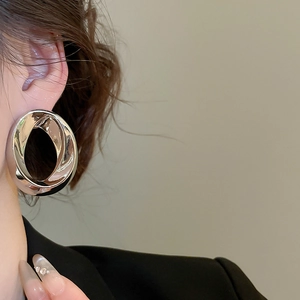 Close-up of a silver-toned oval metal hoop earring worn by a model in black blazer