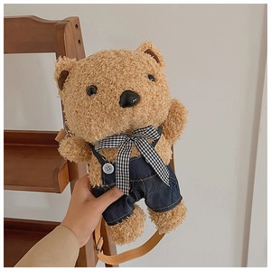 Detail of cute plush teddy bear bag with blue denim overalls and plaid bow strap