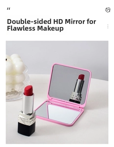 Pink double-sided folding makeup mirror on a vanity with lipstick and candle