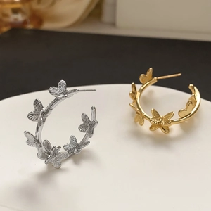 Detail of gold and silver butterfly C-shaped hoop earrings on white display tray